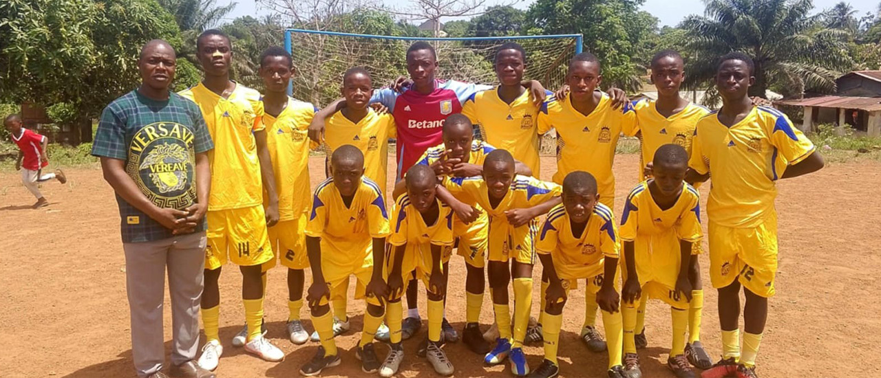 The Kingdom Foundation Institute football team in yellow kit, standing with their coach on the pitch