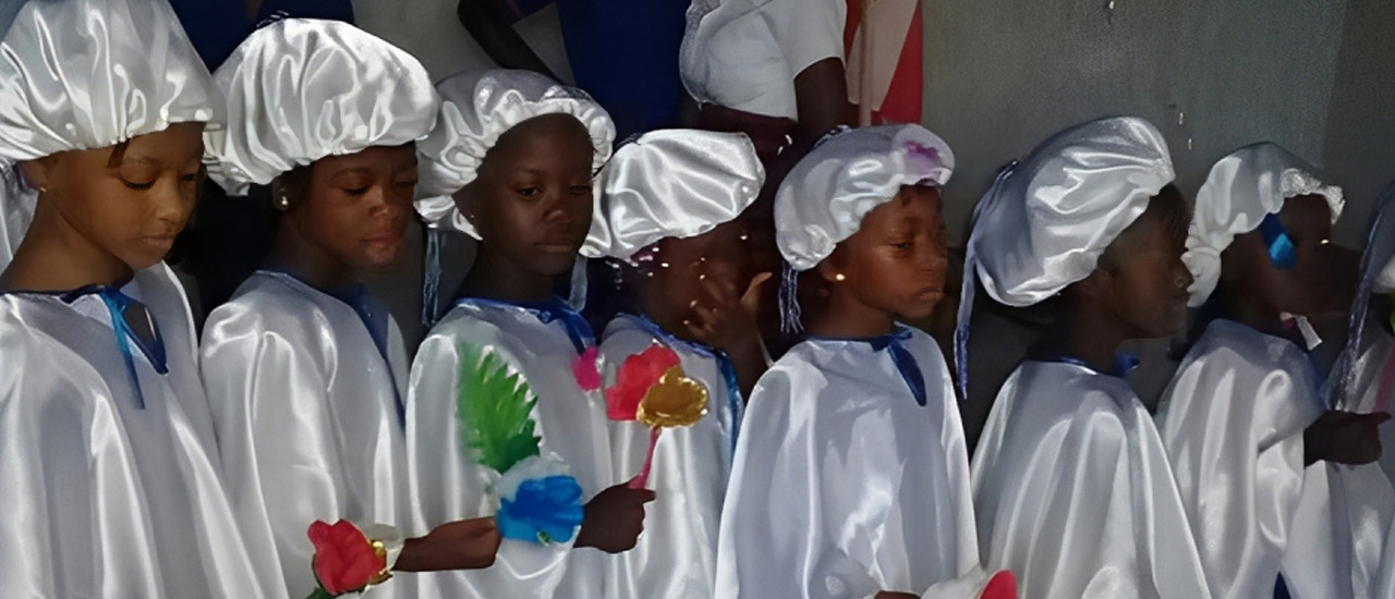 Kingdom Foundation Institute pupils in white ceremonial gowns and caps, holding flowers on graduation day
